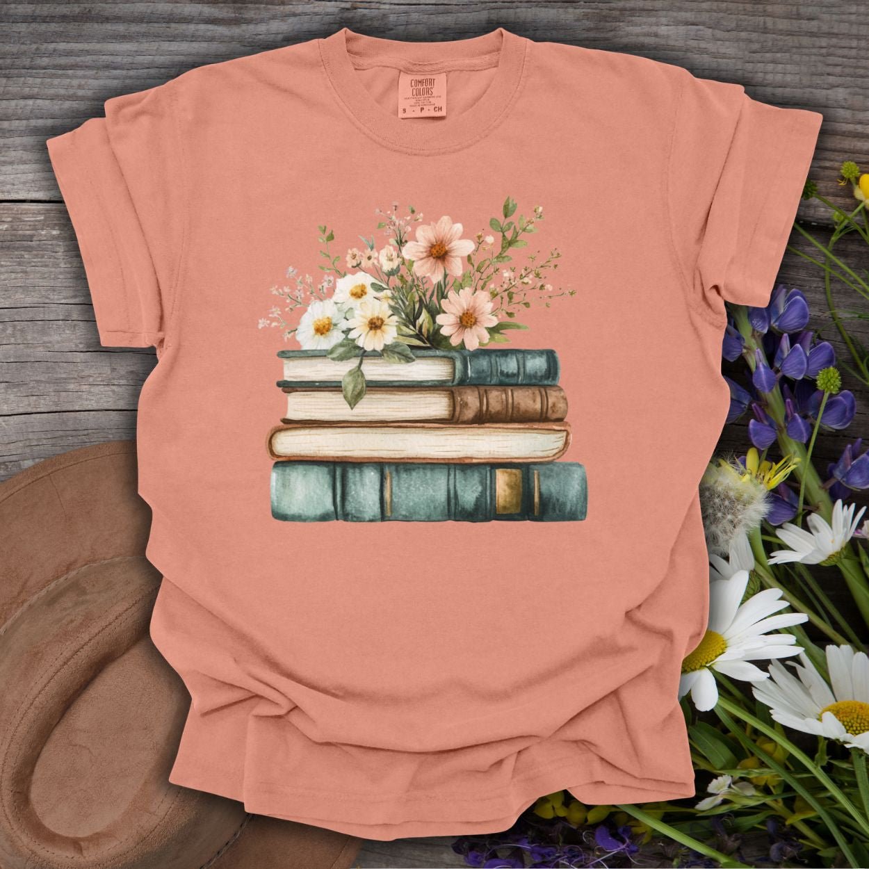 Terracotta S-sized garment-dyed t-shirt with a stacked books and wildflowers illustration.