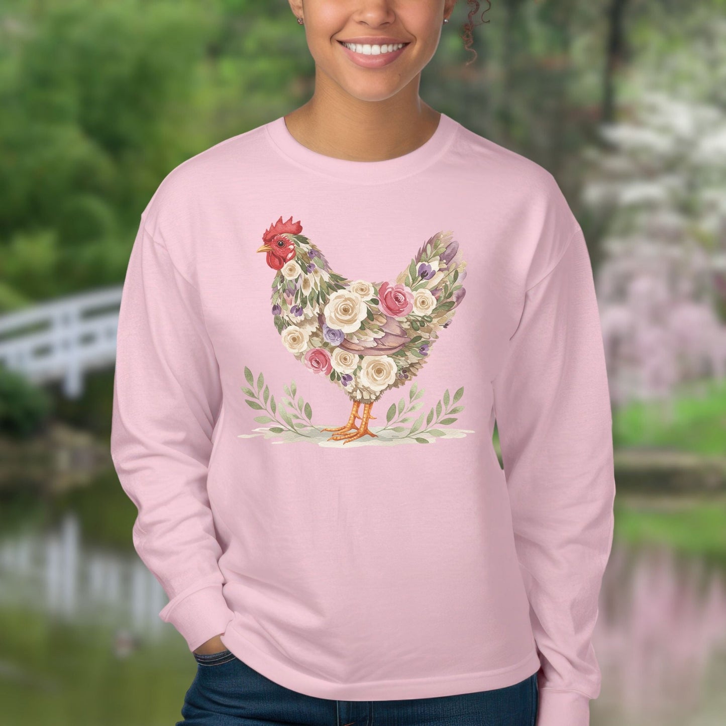 Pink long-sleeve tee with a floral hen design in muted roses and greenery, worn by a smiling person.