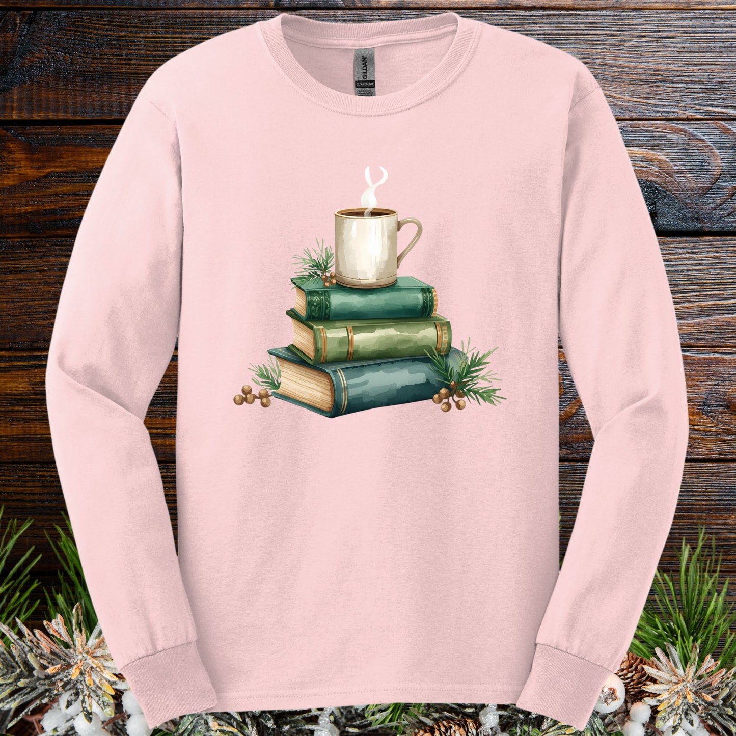 Light pink long sleeve tee with a watercolor design of stacked vintage green books and a steaming coffee mug.