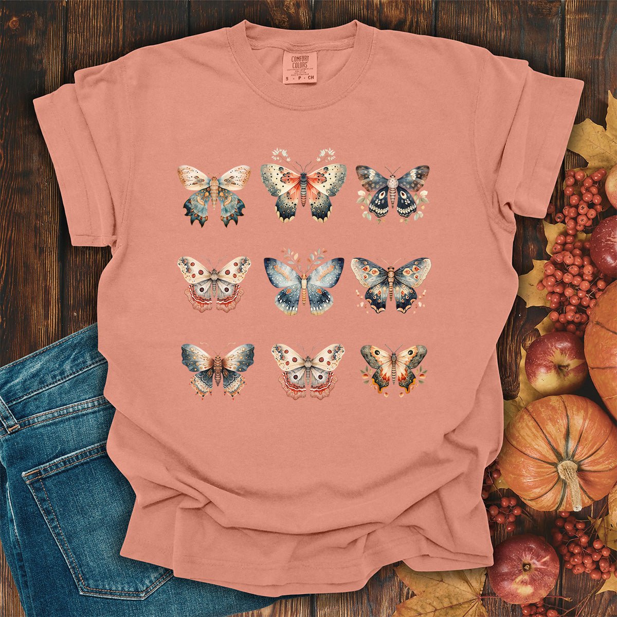 Terracotta garment-dyed cotton t-shirt featuring a grid of vintage watercolor moth and butterfly illustrations.