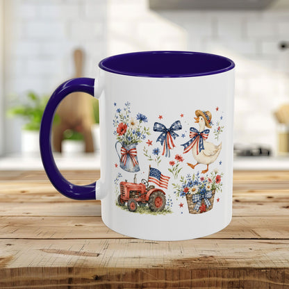 White ceramic mug with purple handle and interior, featuring a patriotic farmhouse design with a goose, tractor, and wildflowers.