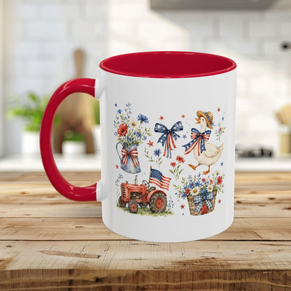 White ceramic mug with red handle and interior, featuring a patriotic farmhouse design with a goose, tractor, and wildflowers.
