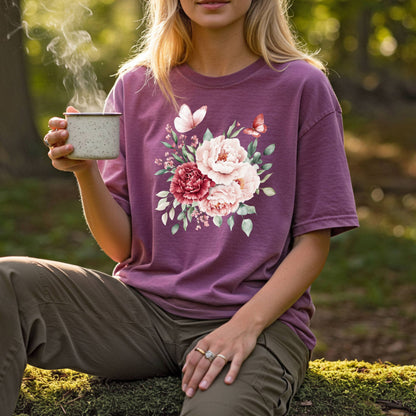 Woman in a relaxed-fit, plum garment-dyed tee with a watercolor peony and butterfly bouquet, holding a steaming mug.