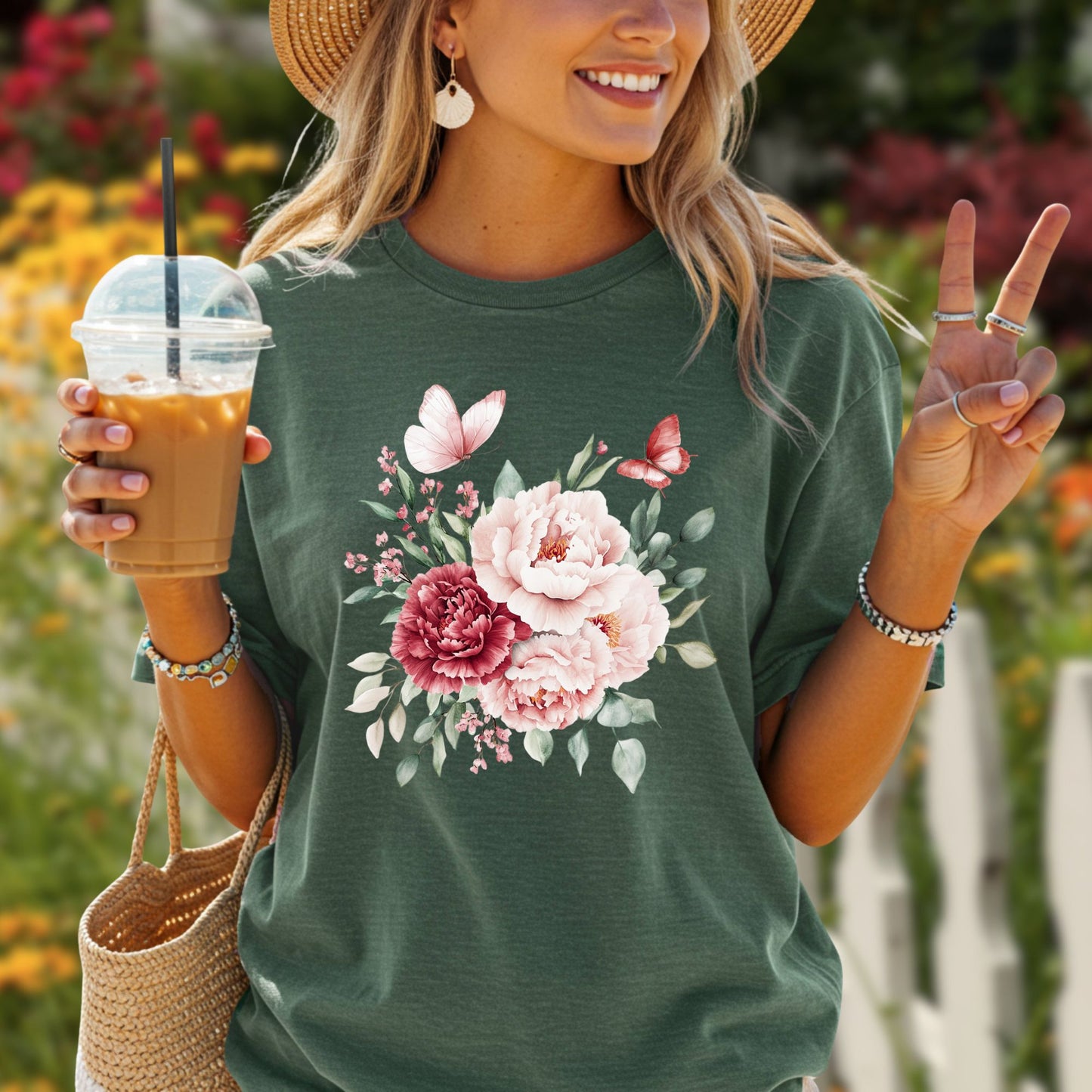 Woman in a dark green vintage peony & butterfly t-shirt, straw hat, holding iced coffee.