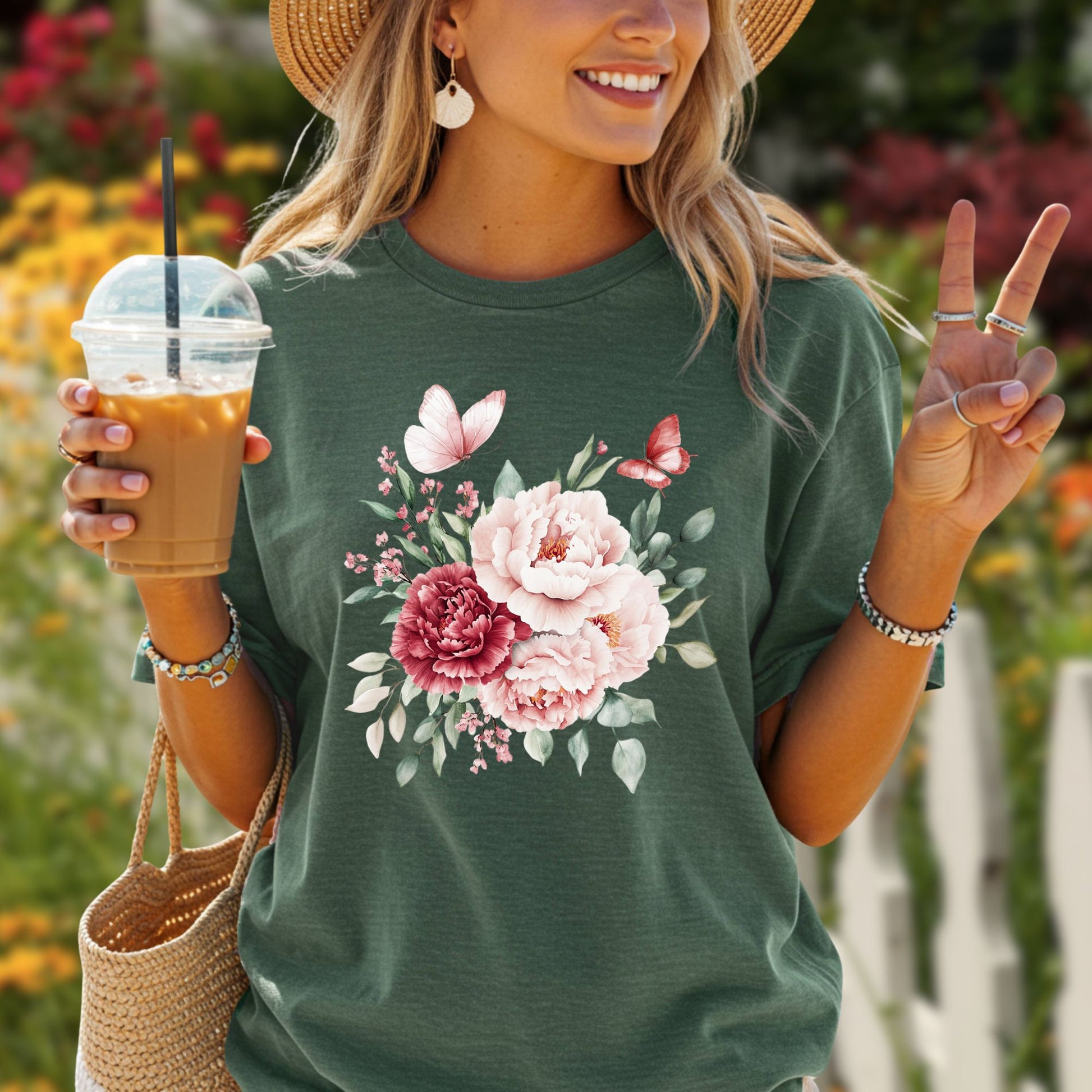 Woman in a dark green vintage peony & butterfly t-shirt, straw hat, holding iced coffee.