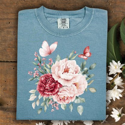 Folded ice blue, garment-dyed cotton t-shirt with a watercolor peony and butterfly bouquet.
