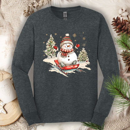 Dark Heather long sleeve tee with a vintage snowman sledding design, surrounded by winter decor.