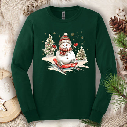 Forest Green Gildan long sleeve tee with a vintage snowman sledding design on a snowy hill.