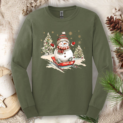 Military Green Gildan 2400 long sleeve tee with a vintage snowman sledding design, surrounded by winter decor.