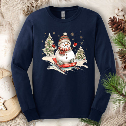 Navy long sleeve tee with a vintage snowman sledding design, surrounded by winter decor.