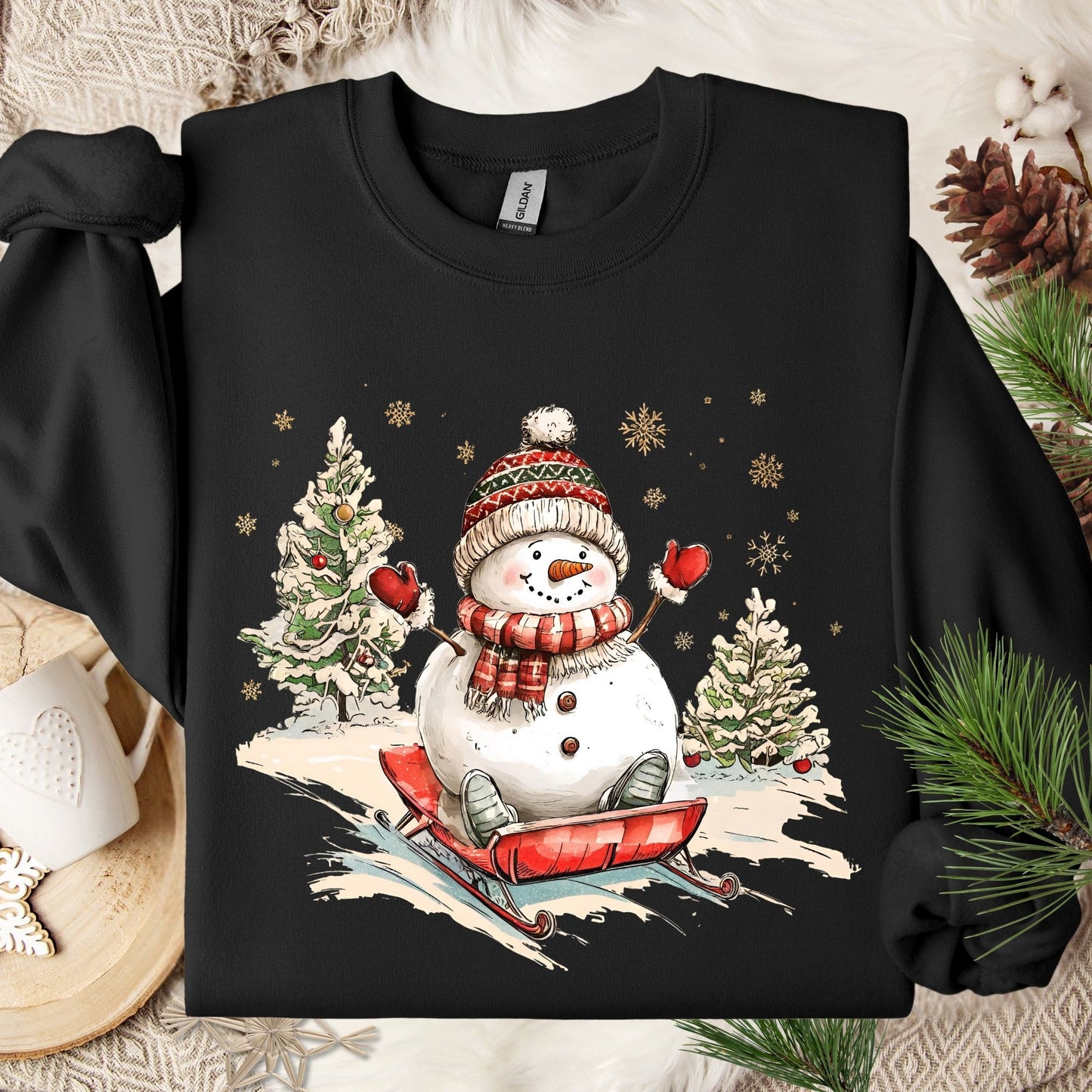 Black Gildan sweatshirt with a vintage snowman sledding design, festive trees, and snowflakes.