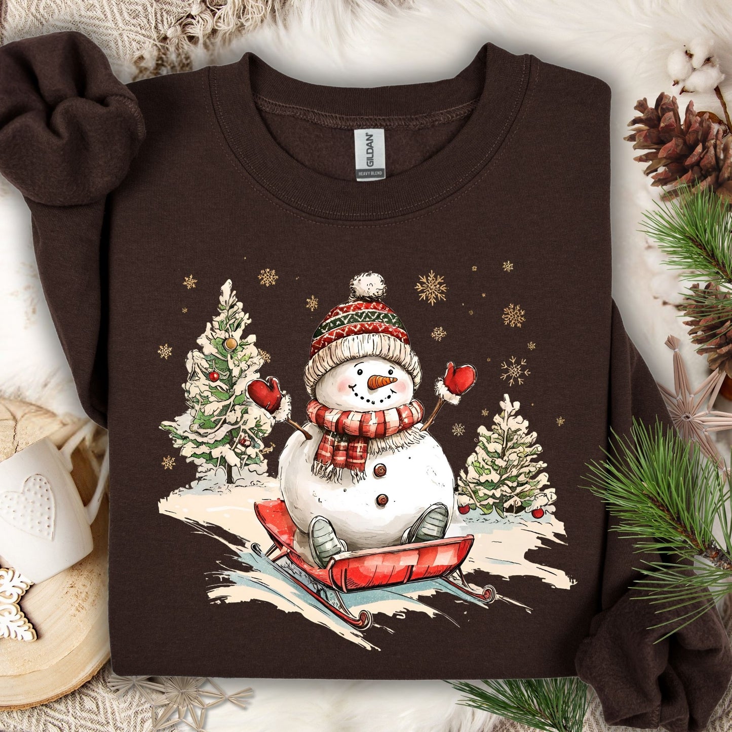 Dark chocolate Gildan sweatshirt with a vintage snowman sledding design, surrounded by winter trees and snowflakes.