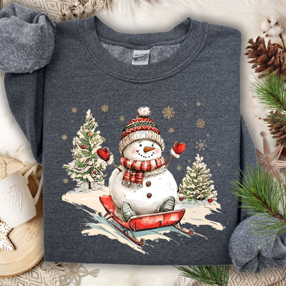 Dark Heather Gildan sweatshirt with a vintage snowman sledding design, surrounded by winter trees and snowflakes.