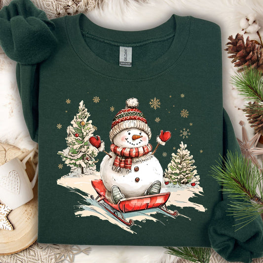 Forest Green Gildan sweatshirt with a vintage snowman sledding design, surrounded by snow-dusted trees and snowflakes.