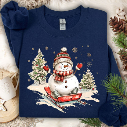 Navy Gildan sweatshirt with a vintage snowman sledding design, surrounded by snowy trees and snowflakes.