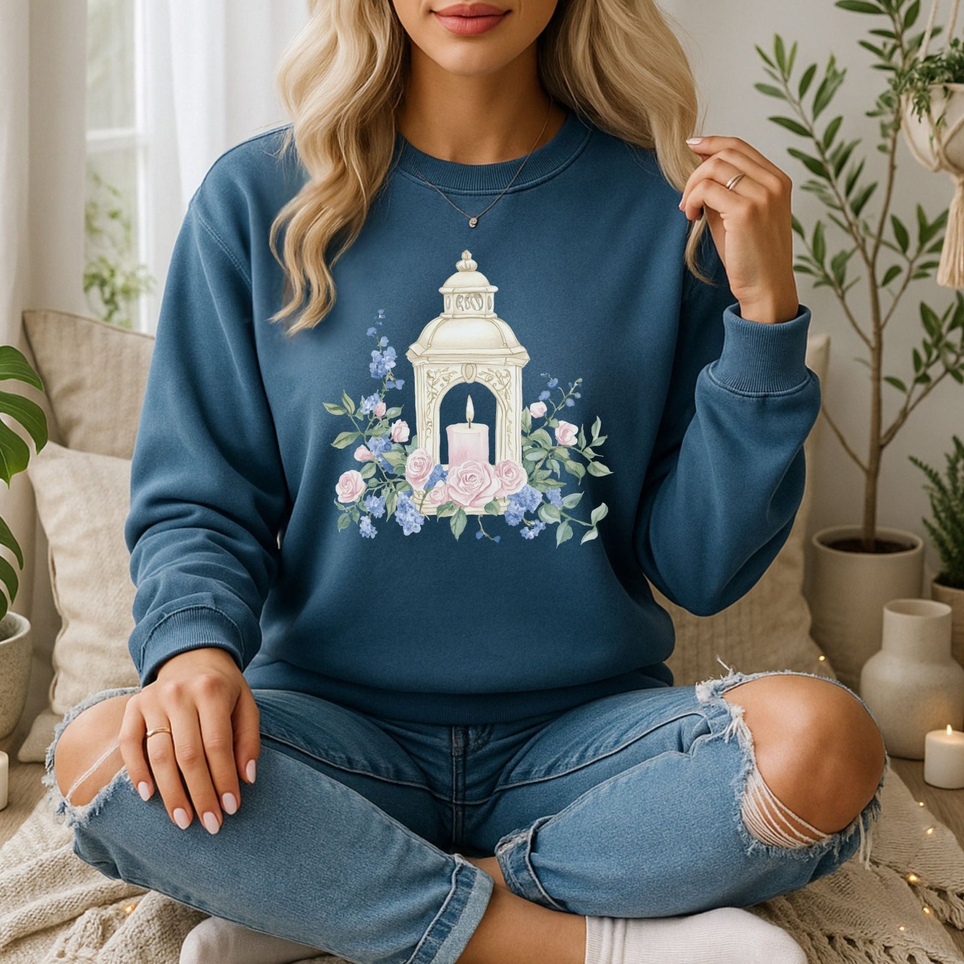 Blonde woman in a blue crewneck sweatshirt with a white lantern, pink candle, and watercolor roses.