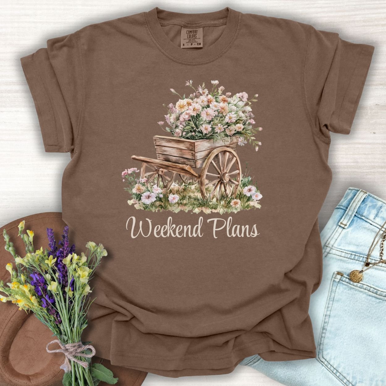 Espresso garment-dyed cotton t-shirt with a watercolor rustic gardening wagon overflowing with carnations and "Weekend Plans" text.