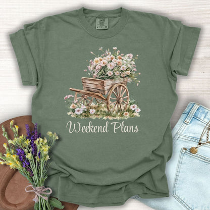 Moss green garment-dyed t-shirt with a watercolor rustic gardening wagon overflowing with pink carnations and "Weekend Plans" text.