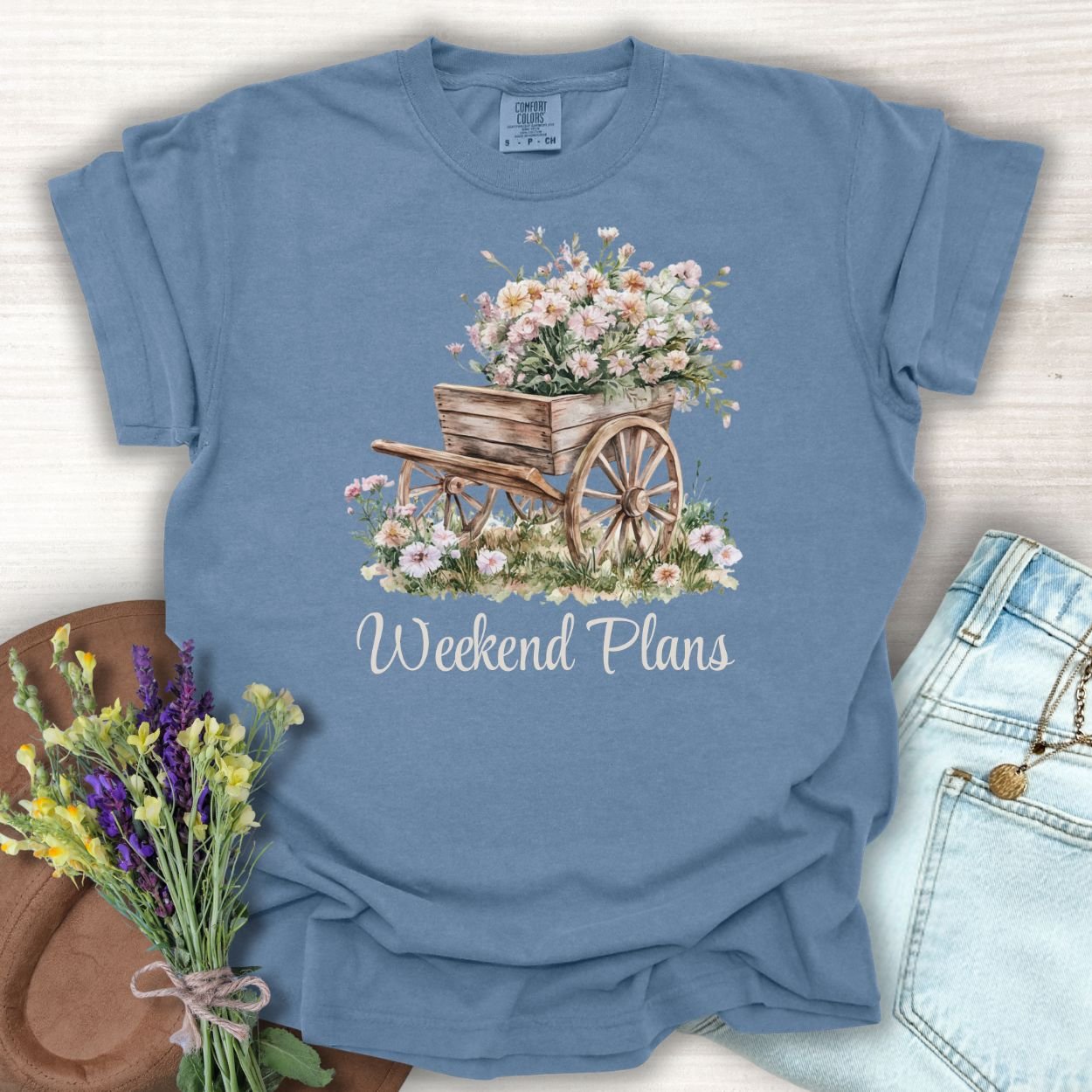 Denim blue cotton t-shirt with a watercolor rustic gardening wagon overflowing with pink carnations and "Weekend Plans" text.