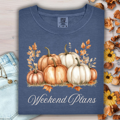 Denim blue heavyweight cotton t-shirt with watercolor pumpkins and "Weekend Plans" text, next to jeans and fall leaves.