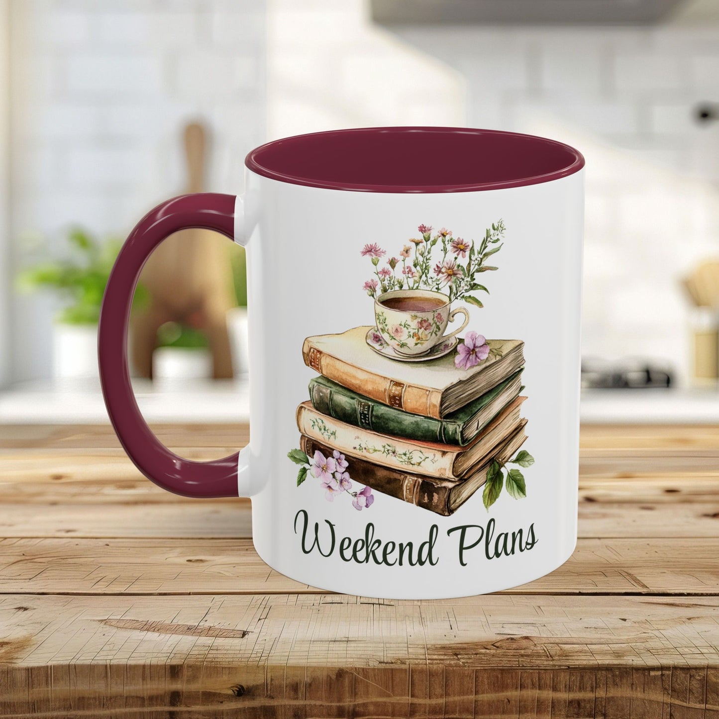 White ceramic mug with a maroon handle and interior, featuring a watercolor stack of books, a floral teacup, and "Weekend Plans" text.