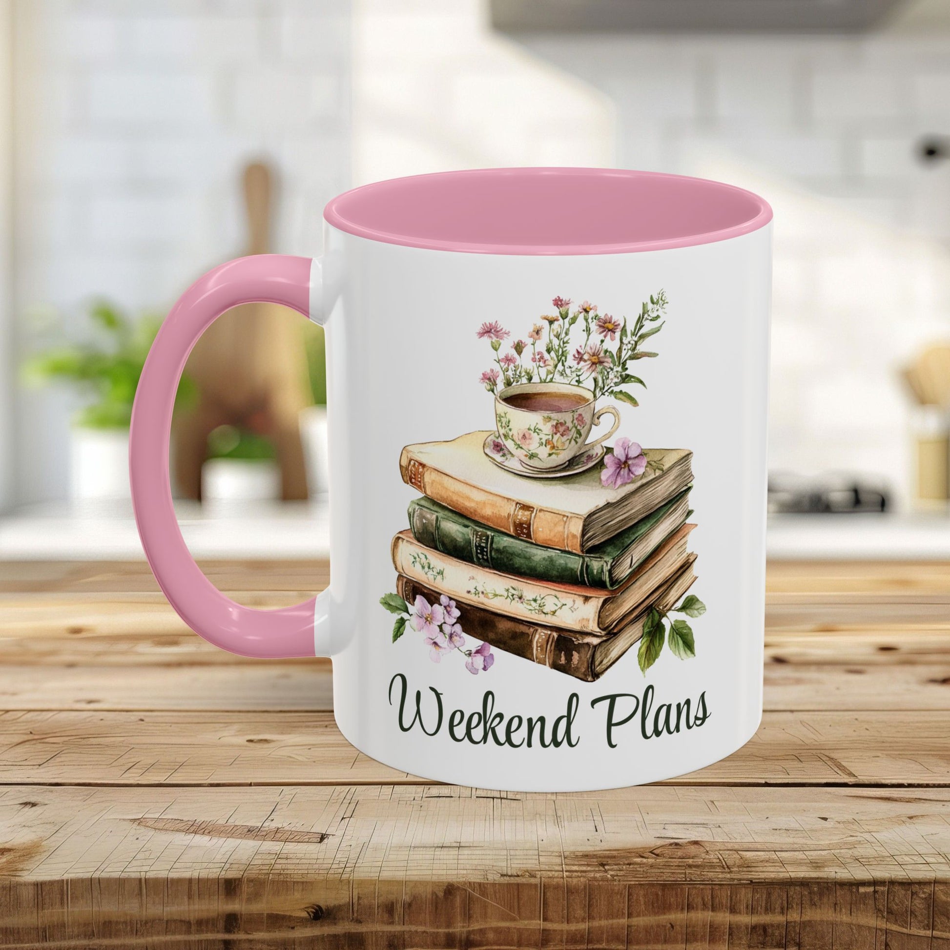 White ceramic mug with pink handle and interior, featuring a watercolor stack of books, teacup, flowers, and "Weekend Plans" text.