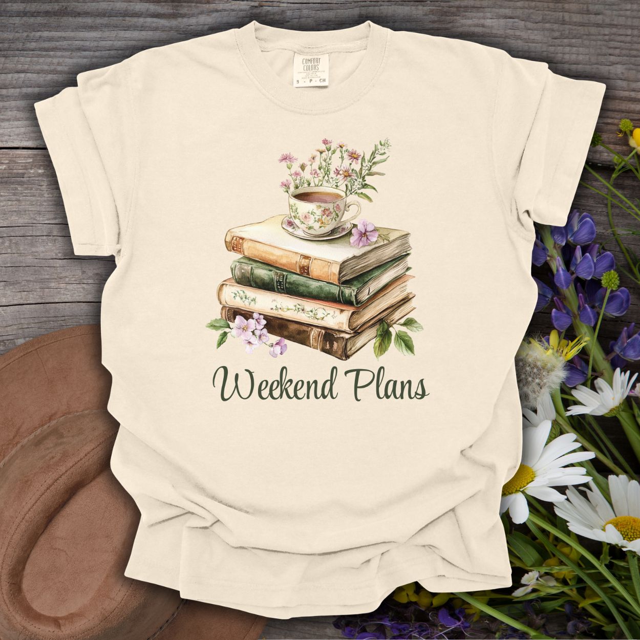 Ivory cotton t-shirt with a watercolor stack of vintage books, a floral teacup, and "Weekend Plans" text.