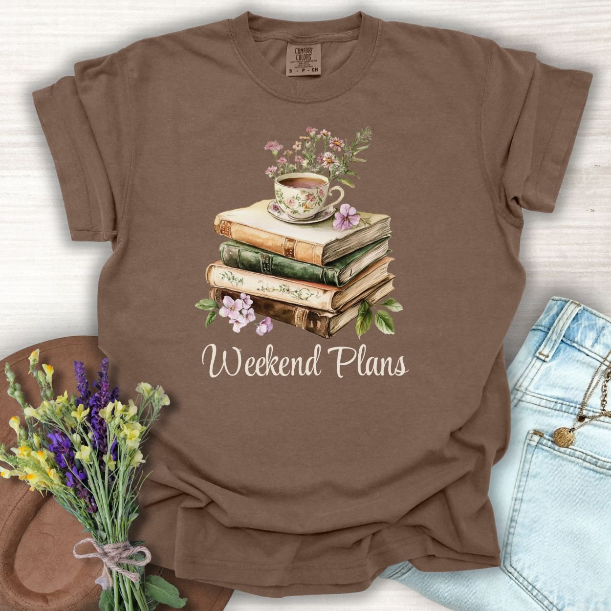 Espresso S-size t-shirt with a watercolor stack of vintage books, floral teacup, and "Weekend Plans" text.