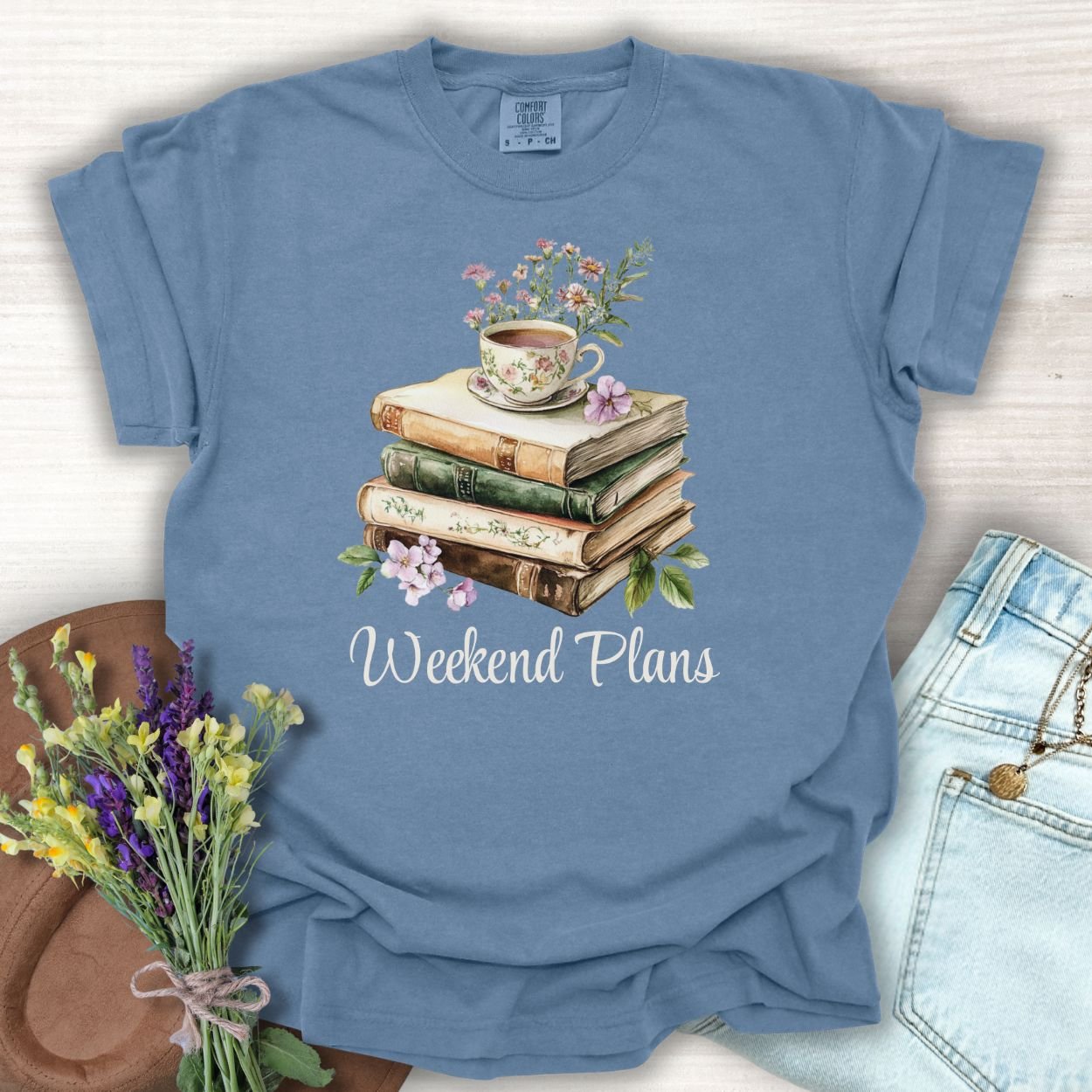 Blue Jean t-shirt with a watercolor stack of vintage books, a floral teacup, and "Weekend Plans" text.