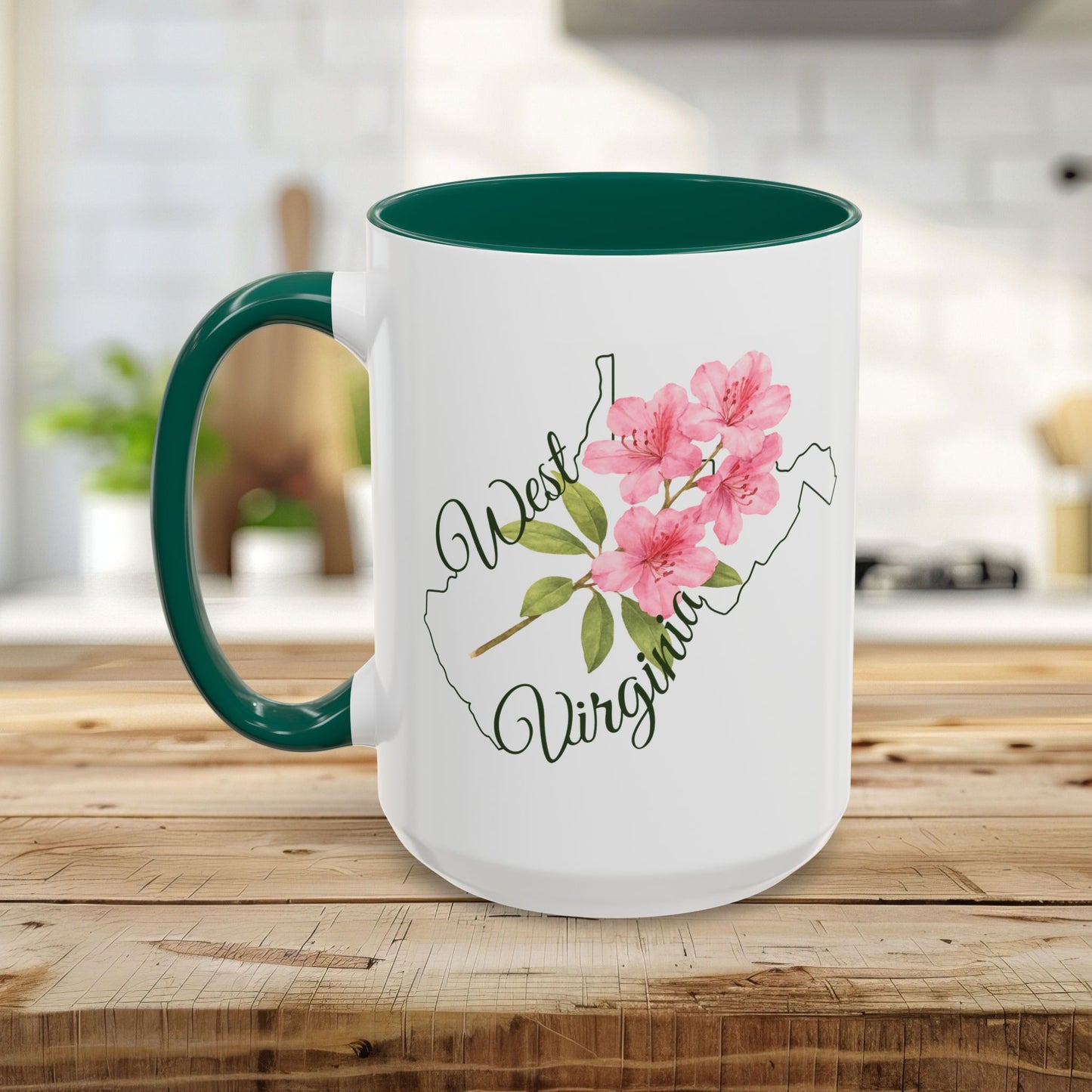 White ceramic mug with green handle/interior, featuring a pink rhododendron and "West Virginia" text over a state silhouette.