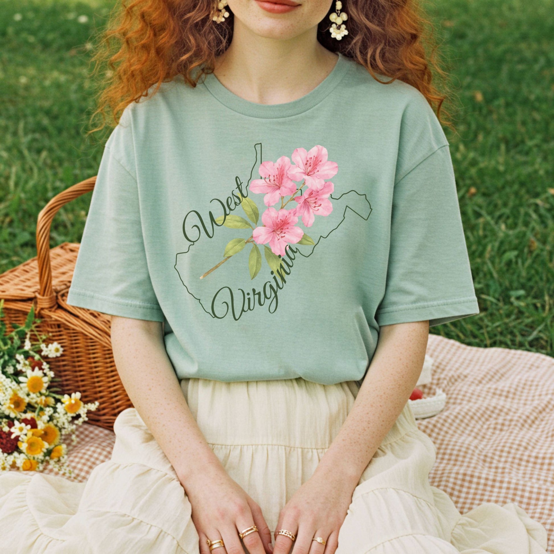 Garment-dyed sage green West Virginia t-shirt with a watercolor rhododendron and state outline.