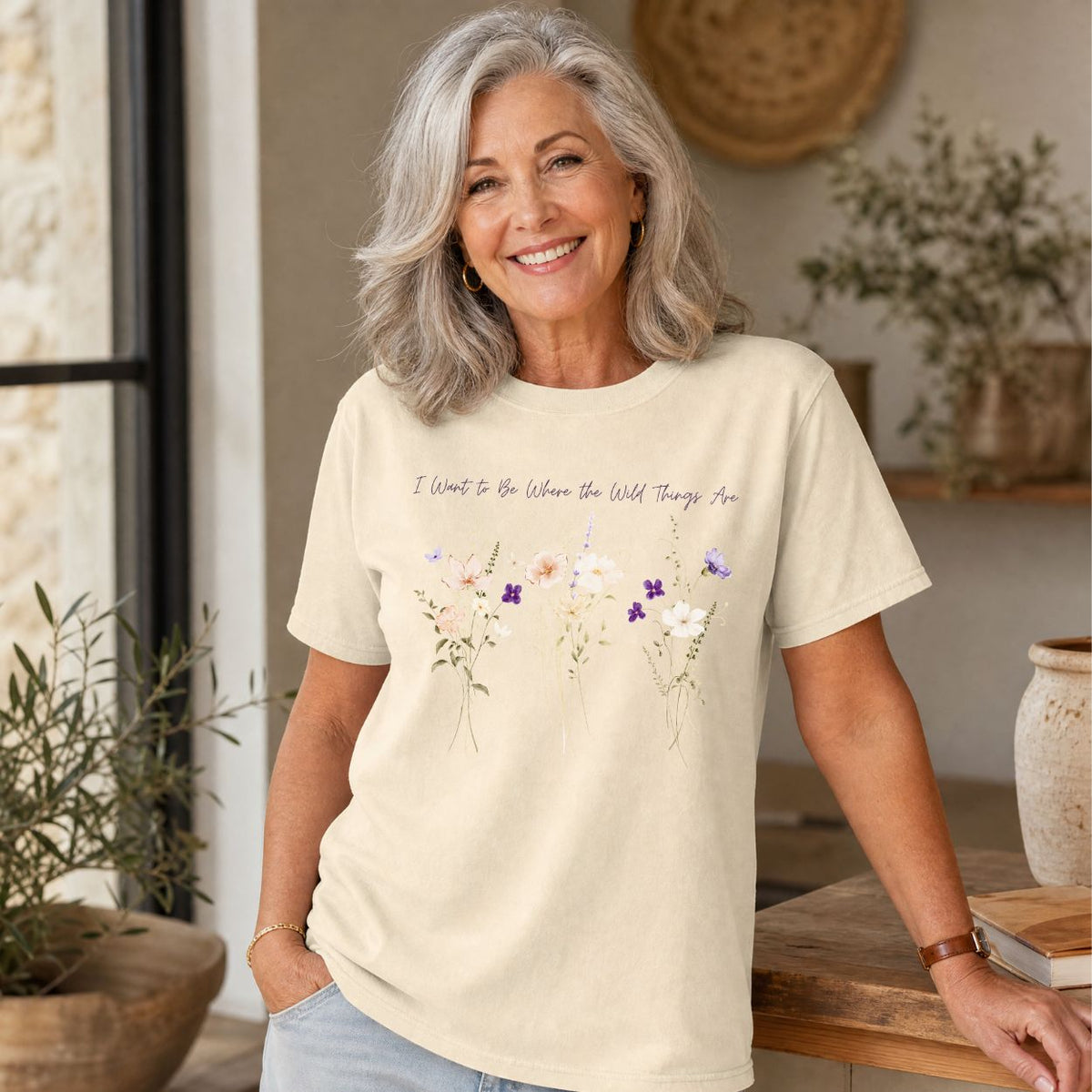 Woman wearing a cream garment-dyed cotton t-shirt with purple watercolor wildflowers and hand-lettered text on the chest.