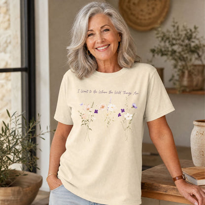 Woman wearing a cream garment-dyed cotton t-shirt with purple watercolor wildflowers and hand-lettered text on the chest.