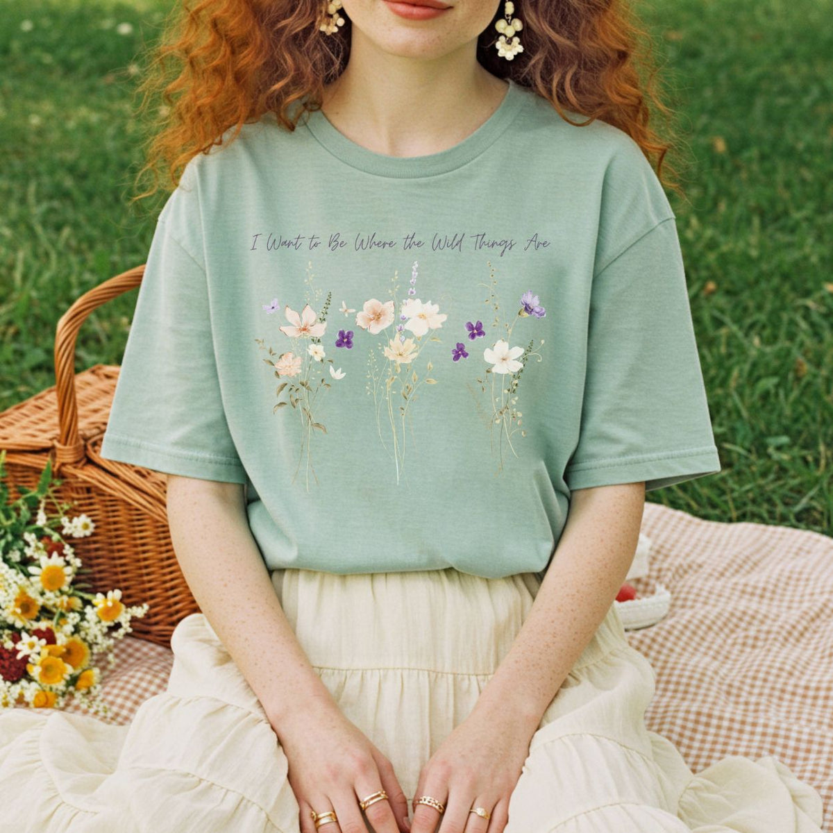 Sage green garment-dyed cotton t-shirt featuring watercolor wildflowers and hand-lettered text on a relaxed-fit crew neck.