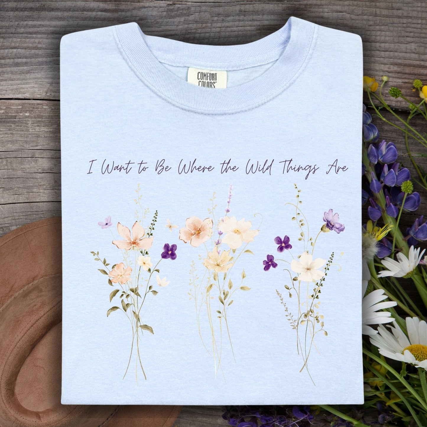 Hydrangea blue Comfort Colors t-shirt with "I Want to Be Where the Wild Things Are" and cream/purple wildflowers.