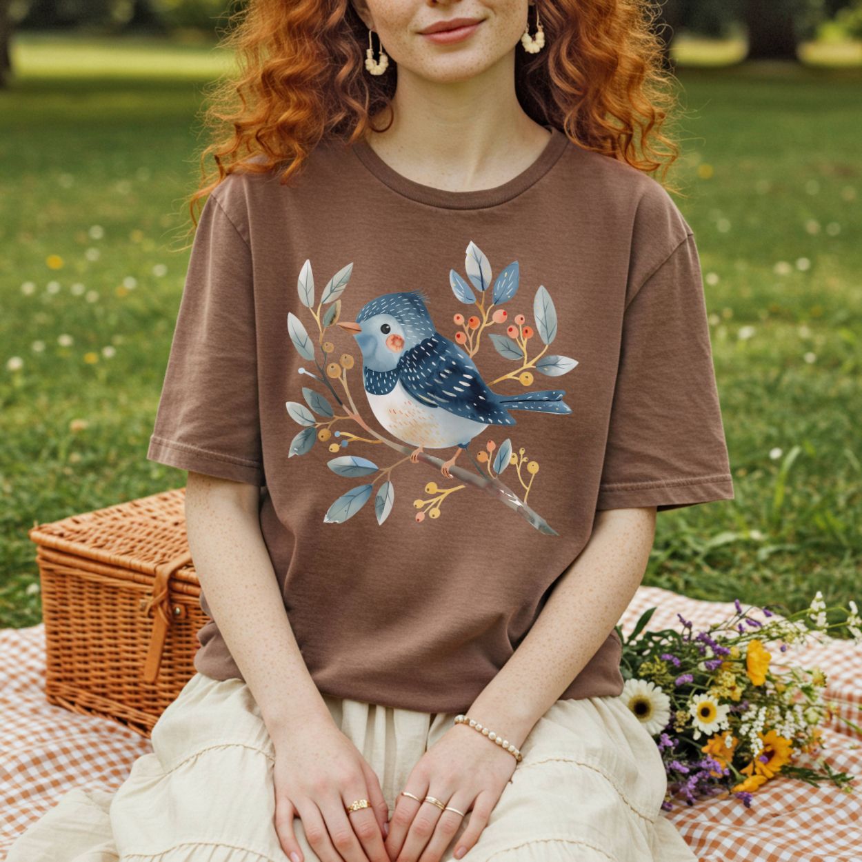 Whimsical bluebird on branch design on a relaxed-fit, garment-dyed brown t-shirt worn by a person outdoors.