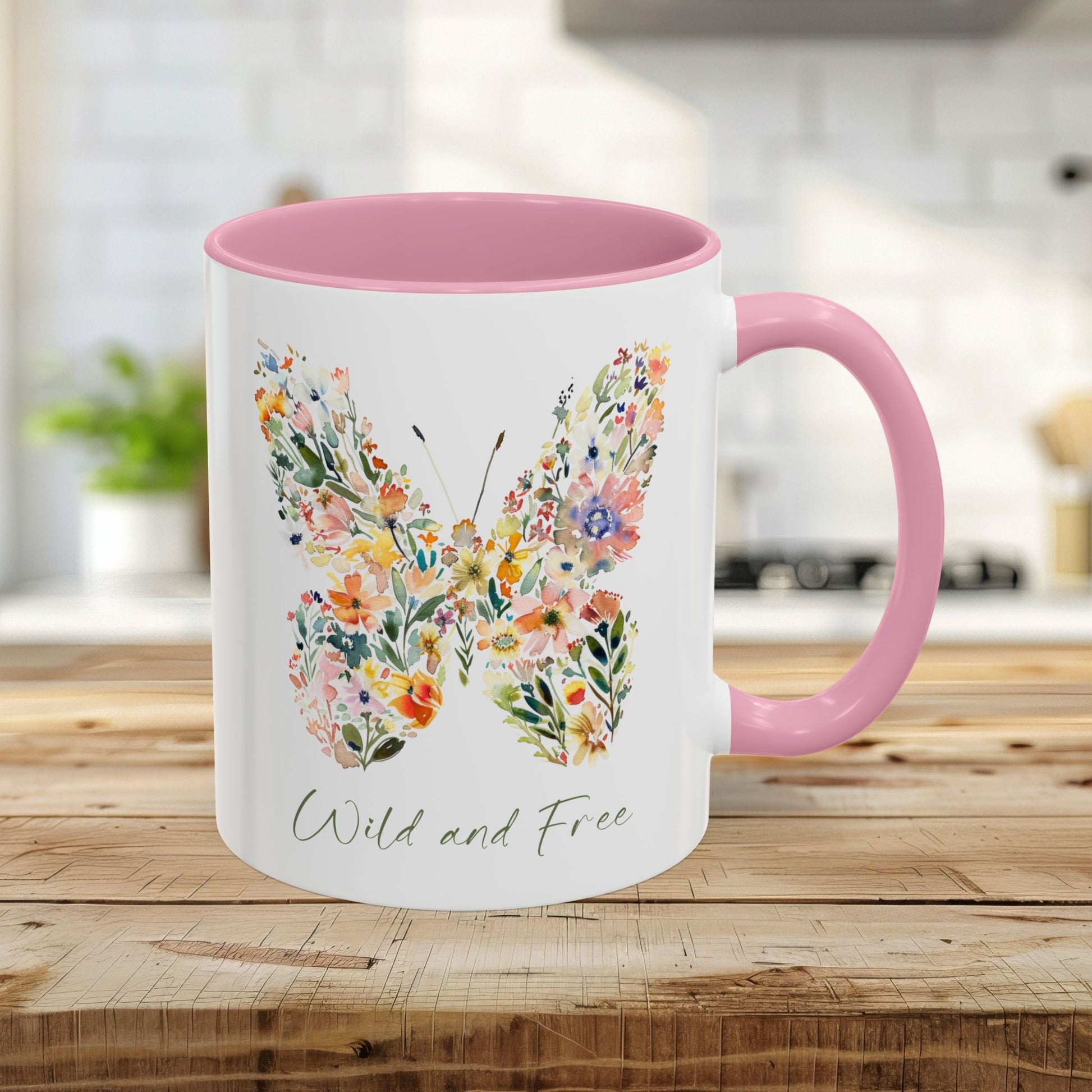 White 11oz ceramic mug with pink interior and handle, featuring a watercolor floral butterfly and "Wild and Free" text.