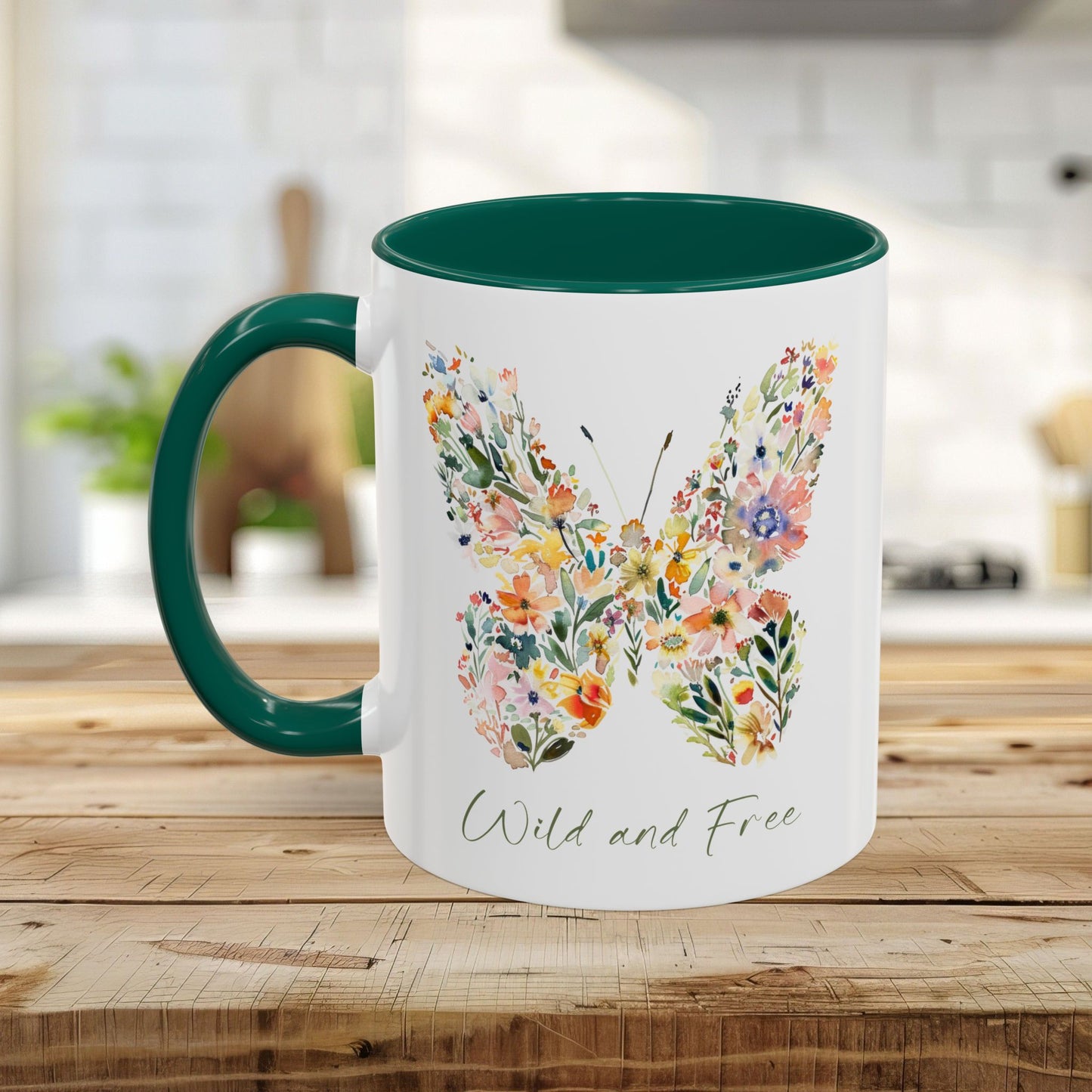 White ceramic mug with a green handle and interior, featuring a watercolor floral butterfly and "Wild and Free" text.