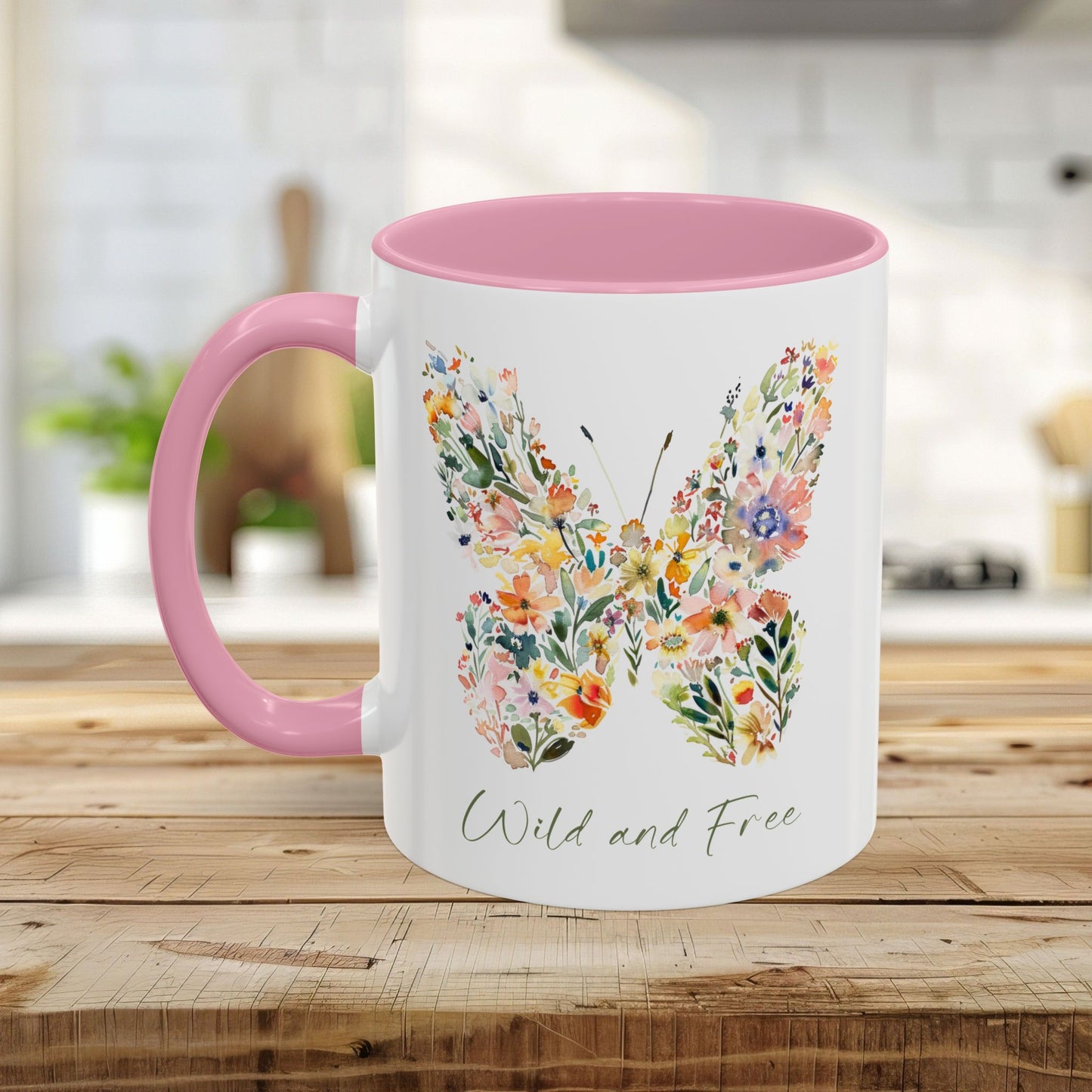 White ceramic mug with pink interior and handle, featuring a watercolor floral butterfly and "Wild and Free" text.
