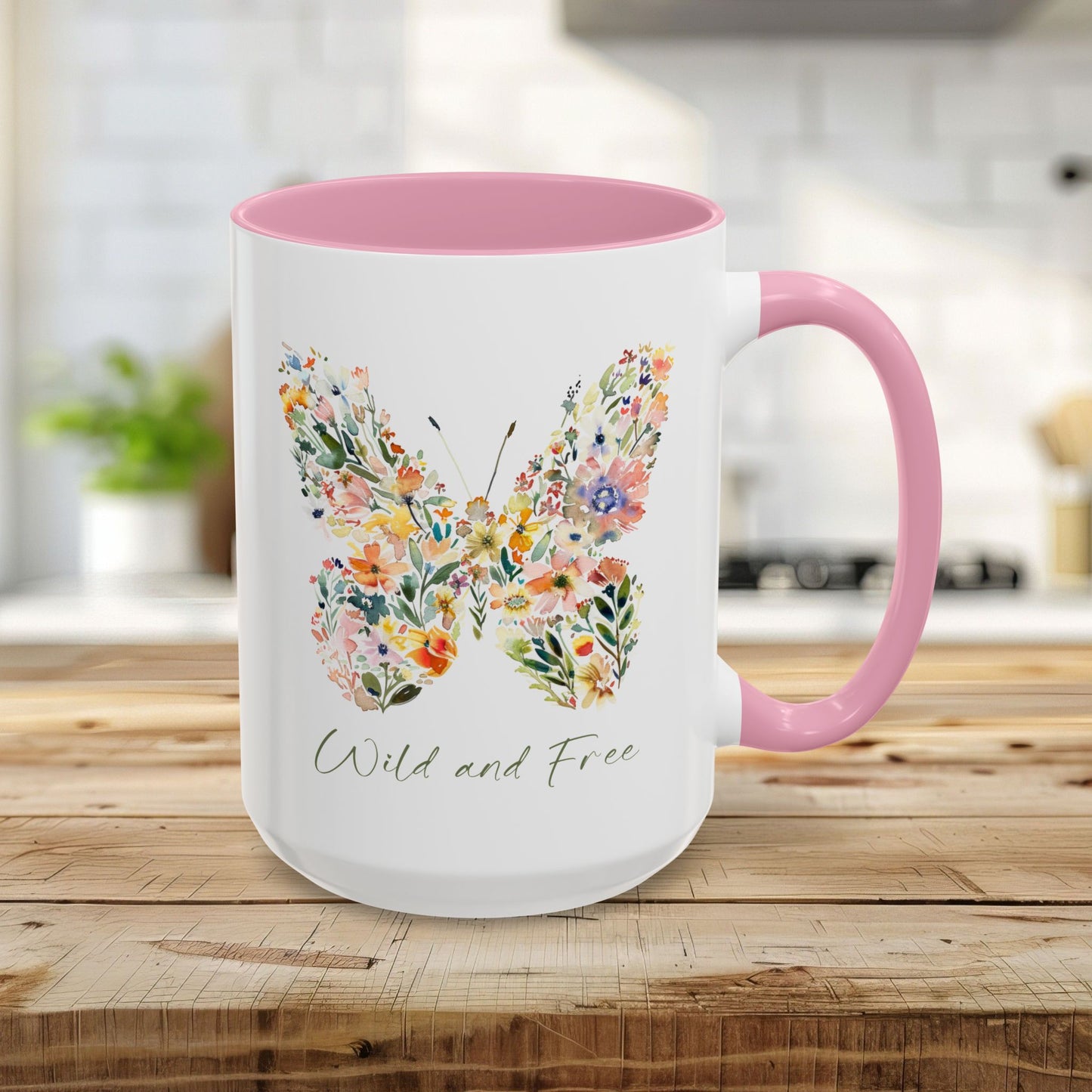 White 15oz ceramic mug with pink interior and handle, featuring a watercolor floral butterfly and "Wild and Free" text.