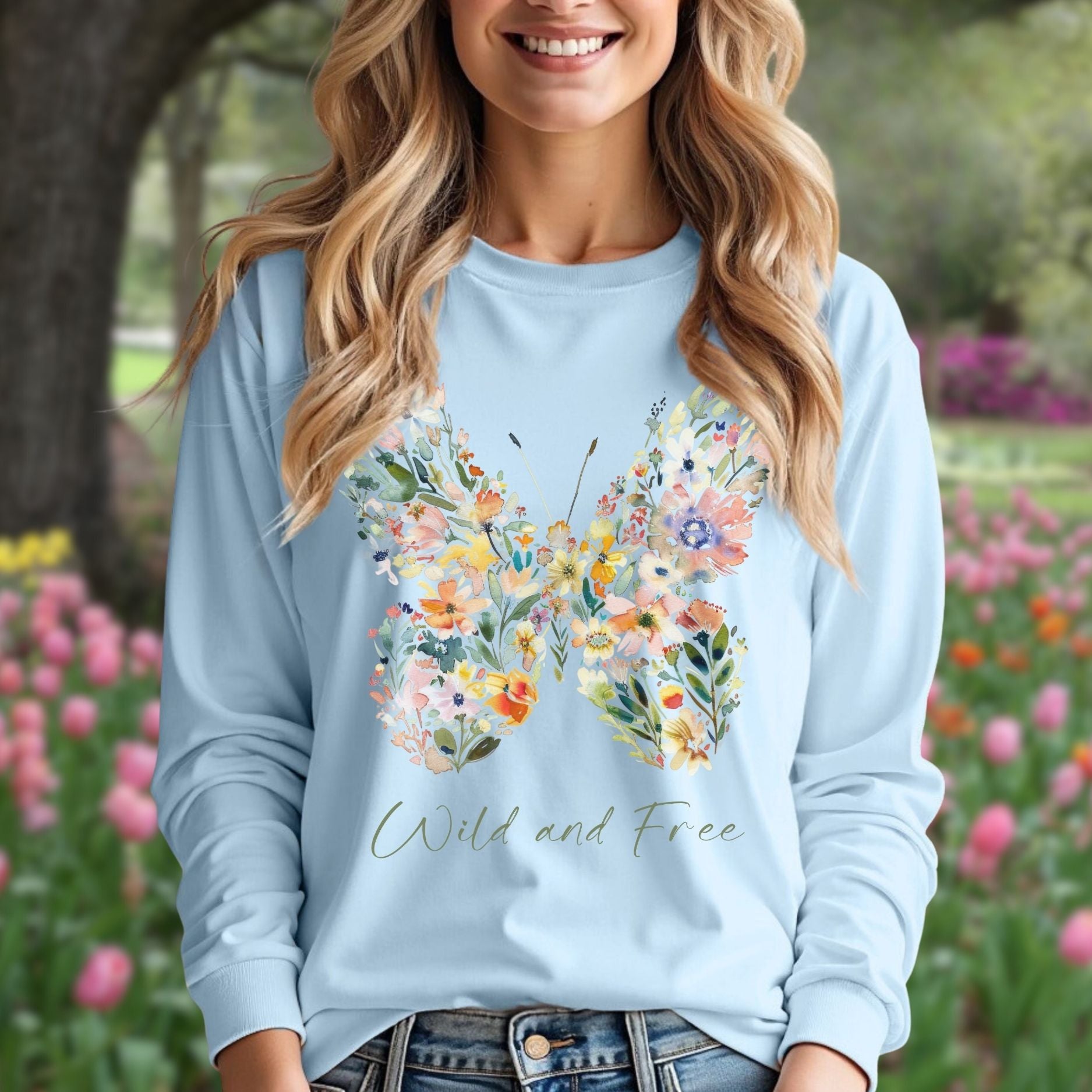 Light blue long-sleeve tee with a watercolor wildflower butterfly and "Wild and Free" text, worn by a smiling woman.