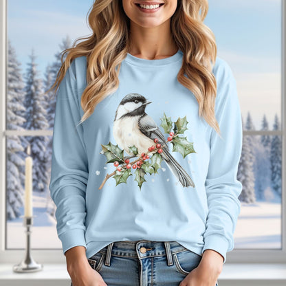 Light blue long sleeve tee with a watercolor chickadee on a snowy holly branch, worn by a smiling woman.