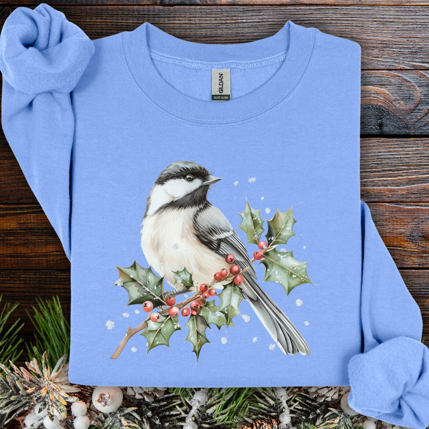 Light blue long sleeve tee with a watercolor chickadee on a snow-dusted holly branch with red berries.