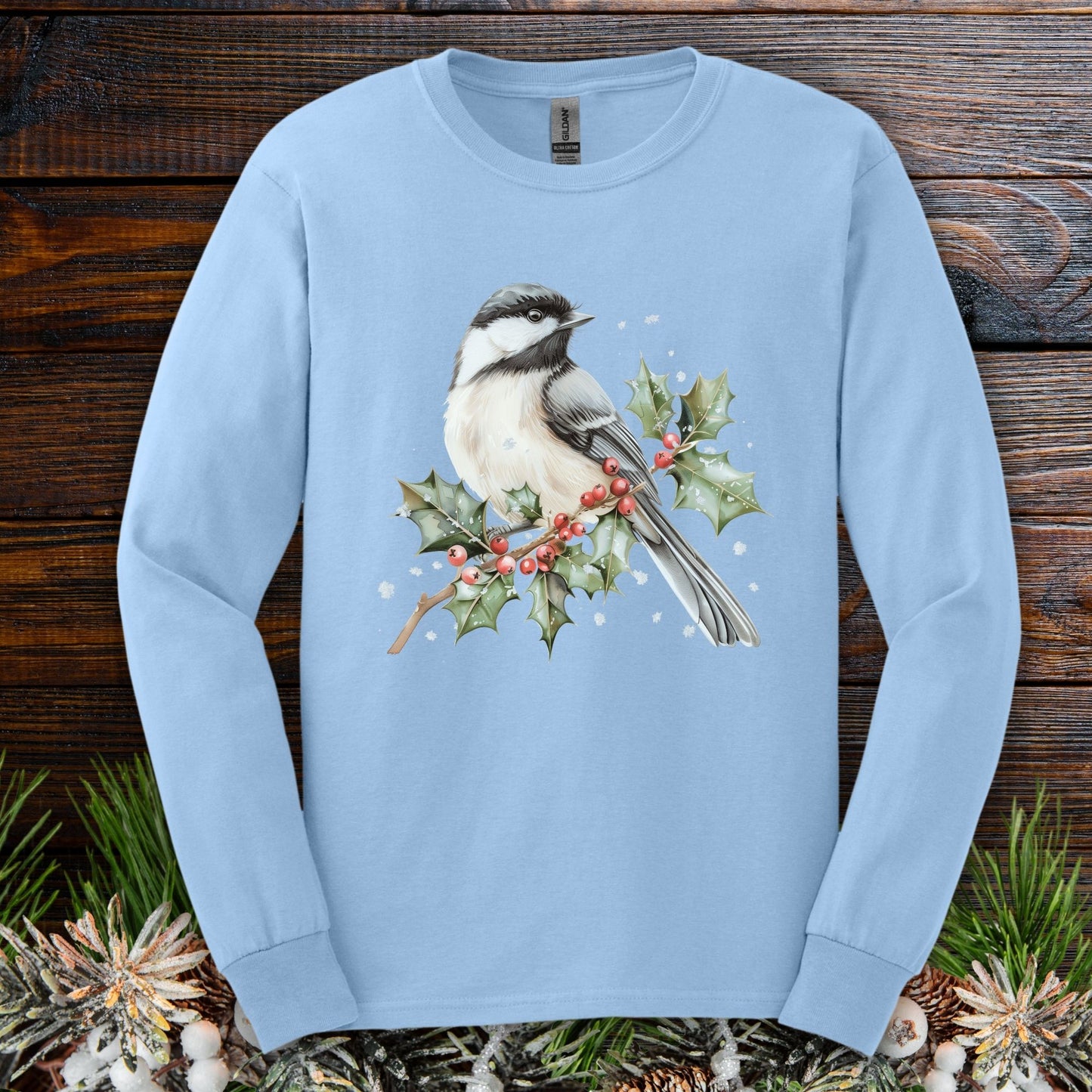 Light blue long sleeve tee with a watercolor chickadee on a snowy holly branch with red berries.