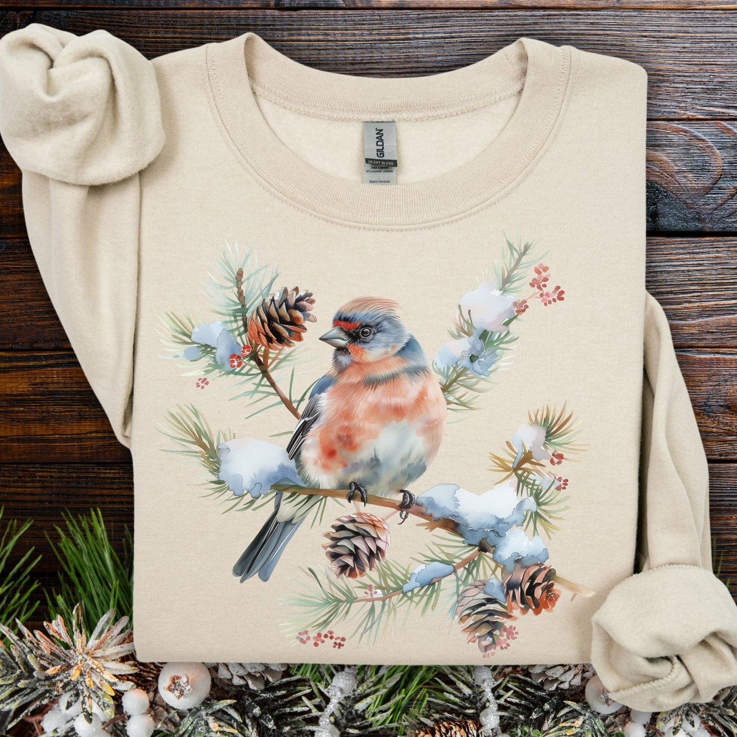 Sand sweatshirt with a winter bird on a snowy evergreen branch, pinecones, and berries design.
