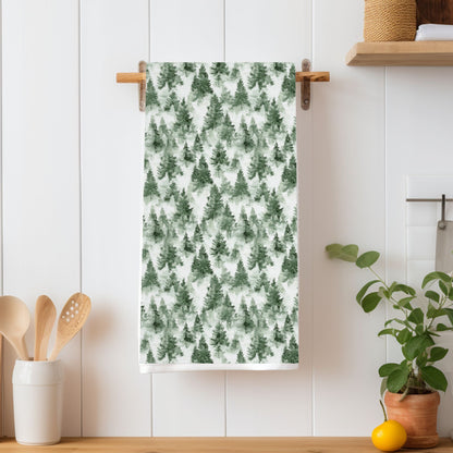 Microfiber tea towel with a painterly evergreen forest pattern hanging on a wooden rack.