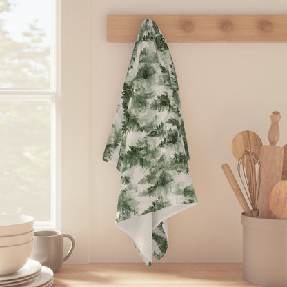 Microfiber tea towel with a painterly green evergreen forest pattern hanging on a wooden hook.
