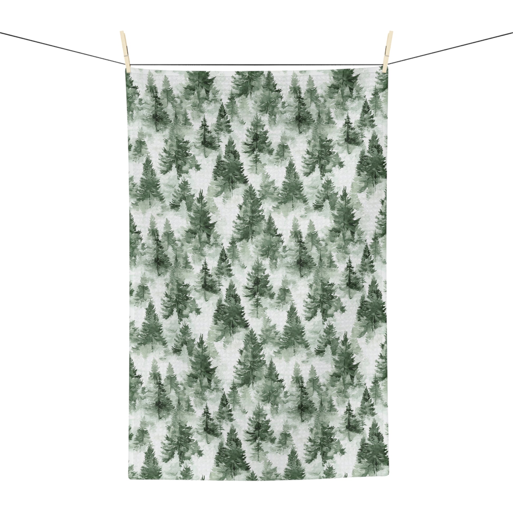 Microfiber tea towel with a painterly deep-green evergreen forest pattern, hanging on a clothesline.