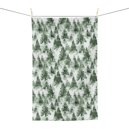 Microfiber tea towel with a painterly deep-green evergreen forest pattern, hanging on a clothesline.