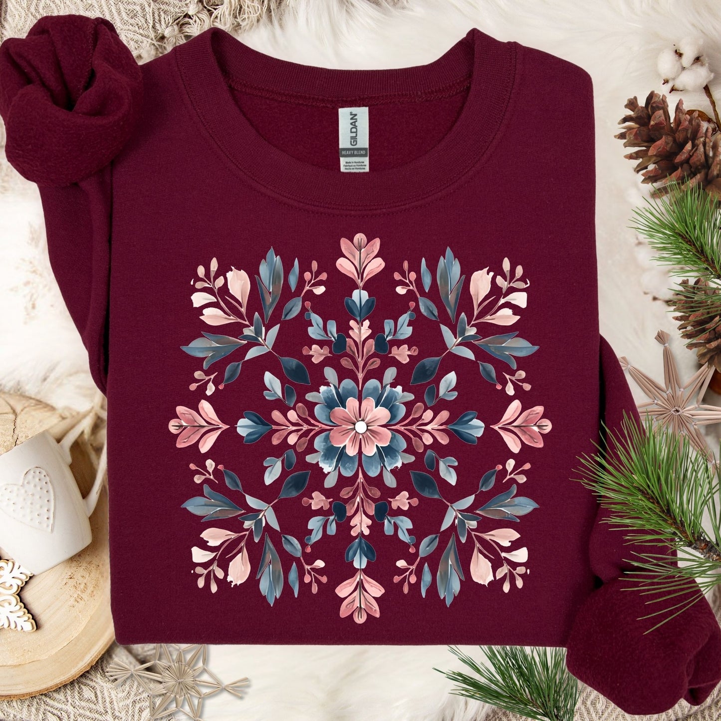 Maroon S sweatshirt with a symmetrical floral snowflake design in pink, blue, and green on a cozy white background.